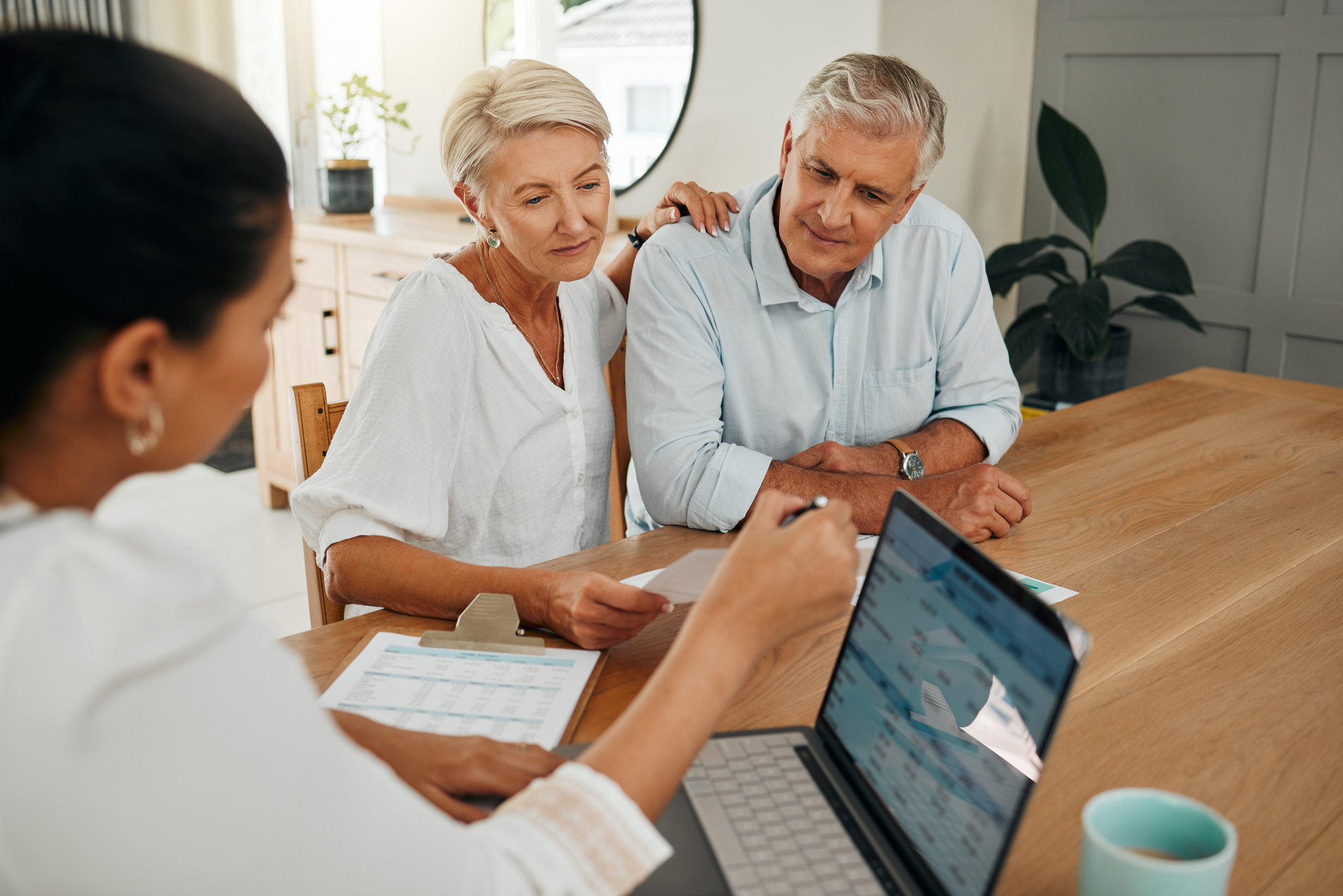 A mature couple sits at a dining table with their financial advisor, discussing market volatility.