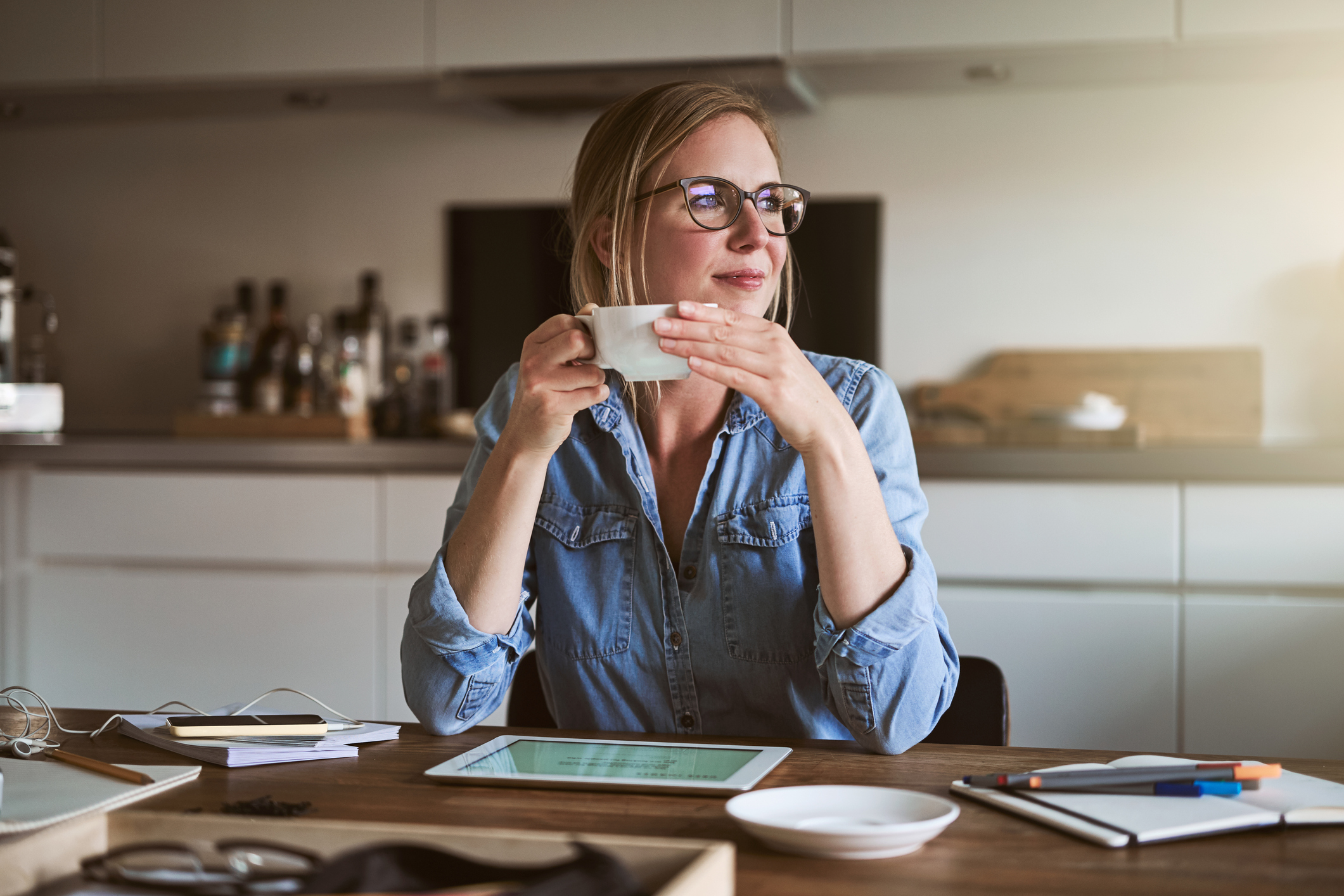 A woman sitting at her kitchen table drinking coffee and reviewing her retirement savings accounts.